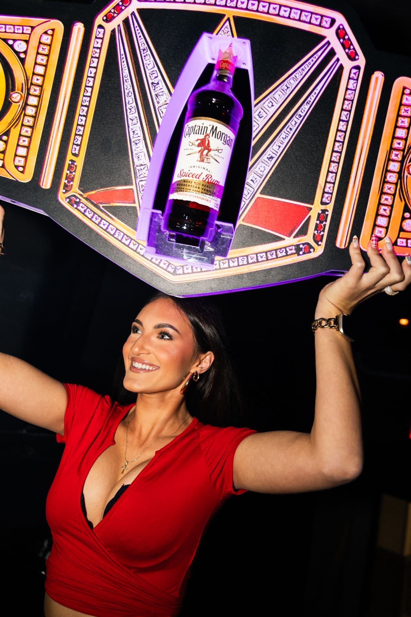 A host raising a champagne bottle in a championship-belt presenter