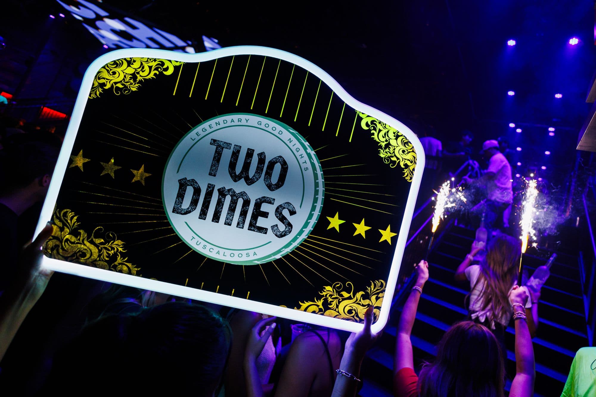 The lit Two Dimes VIP sign and sparklers arriving at a table