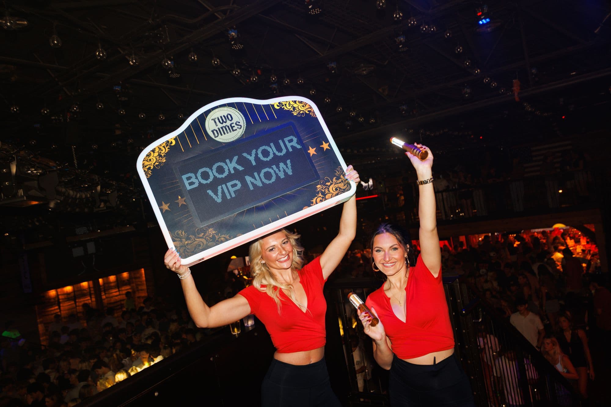 Two Dimes hosts holding a Book Your VIP sign above the crowd
